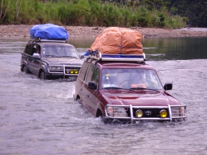 Team trucks carrying supplies across a river as the team moves from village to village